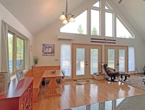 A spacious living room with a wooden bench, a dining table, and a leather chair. There are large windows and a ceiling fan. - Wonderful 3-bedroom house with AC in charming Packwood (Packwood)