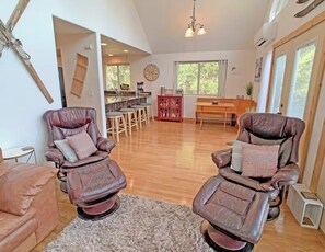 Un vaste espace de vie comprenant deux fauteuils inclinables en cuir, une table à manger en bois et une cuisine située à l’arrière-plan.