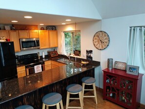 A modern kitchen with wooden cabinets, a black refrigerator, a stainless steel microwave, a large island with stools, and a wall clock. - Wonderful 3-bedroom house with AC in charming Packwood (Packwood)