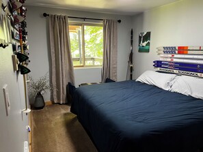 A bedroom with a bed, a window with curtains, a wall-mounted ski rack, and a framed picture. - Wonderful 3-bedroom house with AC in charming Packwood (Packwood)