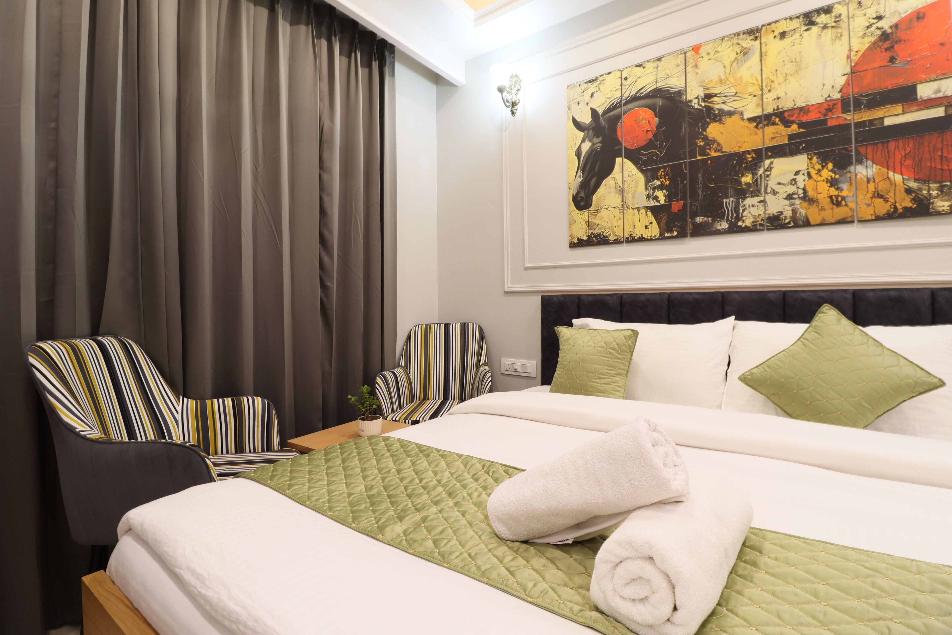 Een hotelkamer met een bed, twee gestreepte fauteuils, een groot abstract schilderij en een raam met gordijnen.