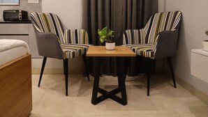 A compact living space with a dining table, two striped chairs, a sofa, a small kitchen area, and a window with curtains. - Exotic Studio Stayz I Artemis Hospital  (Gurugram)