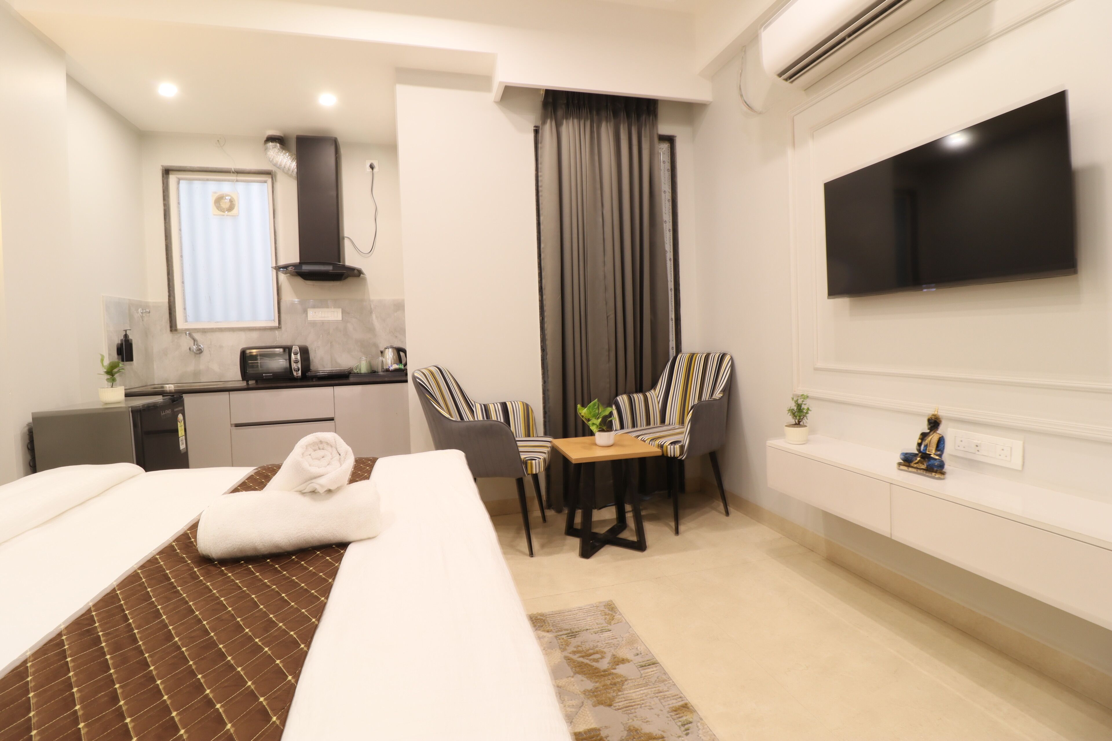 Una habitación de hotel con cama, escritorio, silla, televisor y kitchenette.