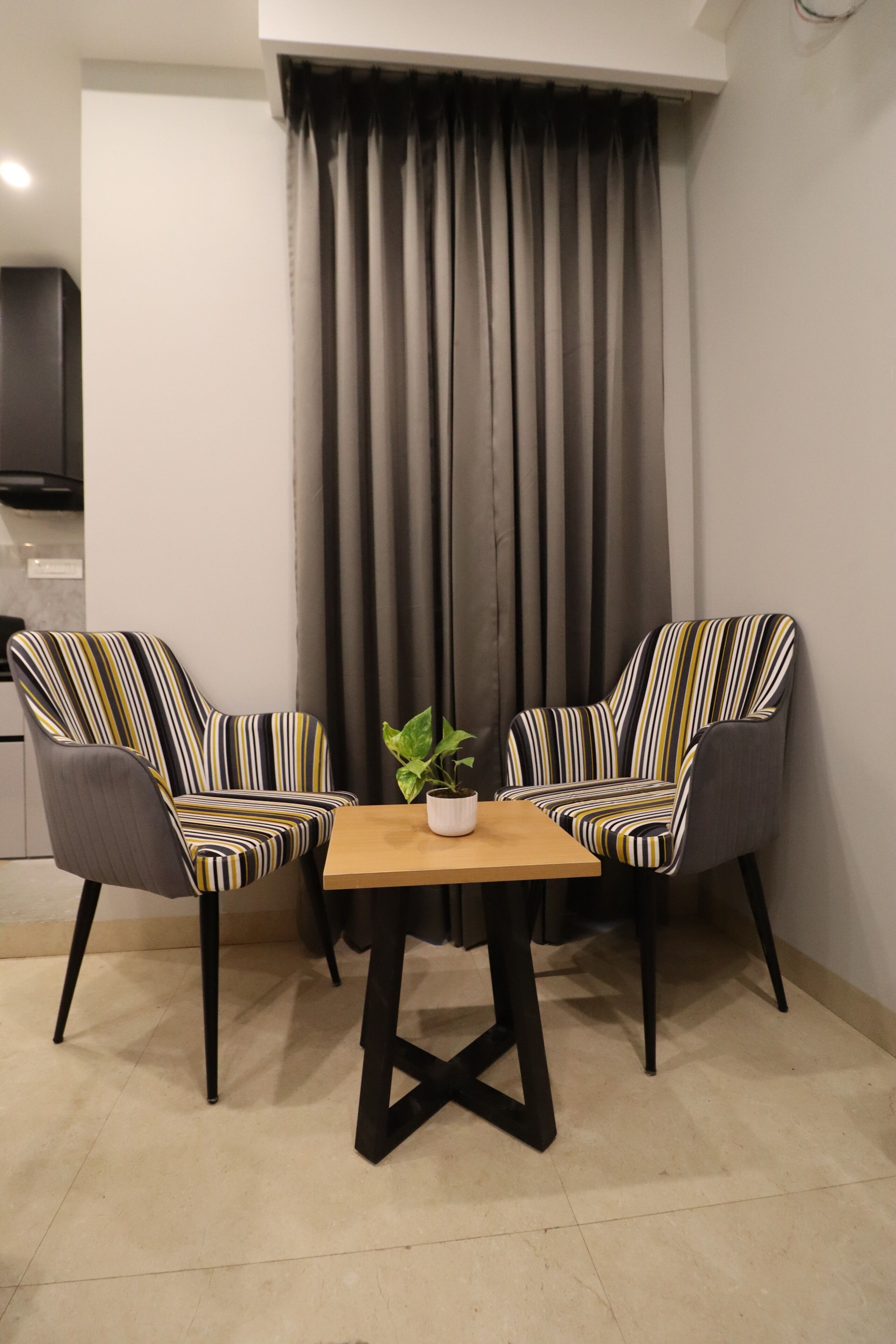 Een kleine kamer met twee gestreept armstoelen, een houten tafel en een potplant.