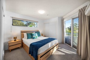 Un dormitorio con cama, mesitas de noche, ventana con vistas y puerta corredera de cristal al exterior.