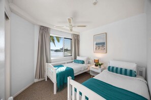 A hotel room with two beds, a window with a view of the sea, a ceiling fan, and a framed picture on the wall. - Charming 2-Bed Coastal Haven Near Esplanade (Maroochydore)
