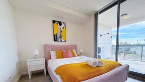 Een moderne slaapkamer met een groot bed, een nachtkastje, een schilderij en uitzicht op het groen.