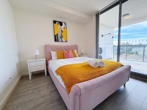 A modern bedroom with a large bed, a nightstand, a painting, and a view of the outdoors. - Luxury 1BR Escape in Heart of Parramatta (Parramatta)