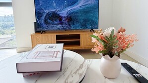 Een woonkamer met een televisie op een houten standaard, een boek op een marmeren tafel en een vaas met bloemen.