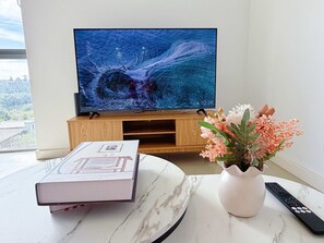 A living room with a television on a wooden stand, a book on a marble table, and a vase with flowers. - Luxury 1BR Escape in Heart of Parramatta (Parramatta)