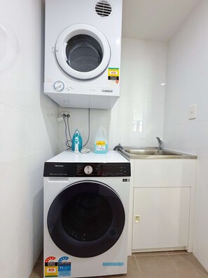 A compact laundry room with a front-loading washing machine and a top-loading dryer. - Luxury 1BR Escape in Heart of Parramatta (Parramatta)