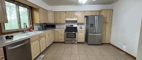 A kitchen with wooden cabinets, stainless steel appliances, a microwave, a refrigerator, and a ceiling fan.
