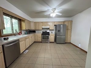 A kitchen with wooden cabinets, stainless steel appliances, a microwave, a refrigerator, and a ceiling fan.
