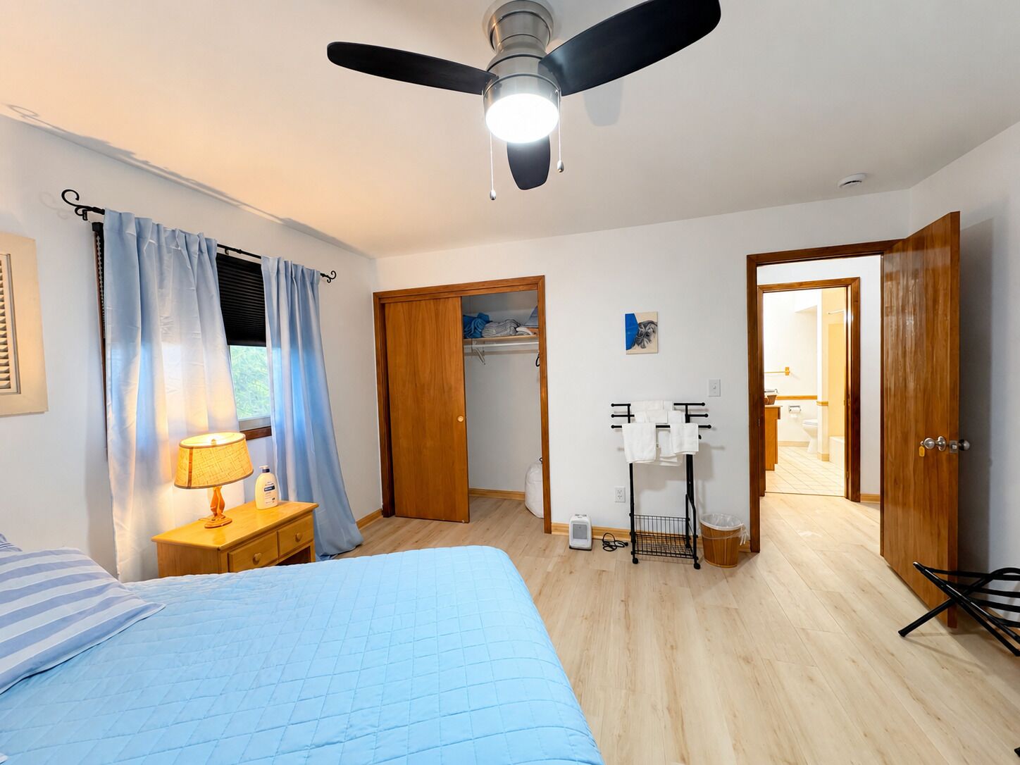 A bedroom with a bed, a bedside table with a lamp, a ceiling fan, and a wardrobe.