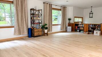 Una habitación amplia con ventanas grandes, un ventilador de techo, una estantería y un pequeño escritorio con una planta.