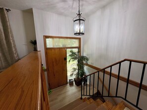 Una escalera de madera con barandilla de metal negro que conduce a una puerta con panel de vidrio.