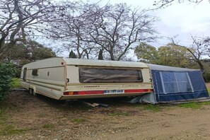 A caravan parked in a wooded area with a blue tent nearby. - Large Tabbert trailer located near the sea in Hyères—secure Beldemé campground (Hyères)
