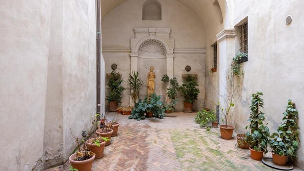 Ein Innenhof mit einer Statue, Blumentöpfen und einem Fischgrätparkettboden.