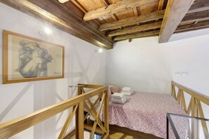 Ein Zimmer mit Holzbalkendecke, einem Bett mit gemustertem Bettbezug, einem gerahmten Kunstwerk an der Wand und einem Glasgeländer.
