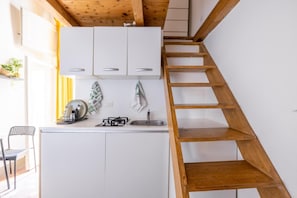 A compact kitchen with white cabinets, a gas stove, and a wooden ladder. - Little House in Trastevere Apartment with Balcony, Wi-Fi and Air Conditioning (Rome)