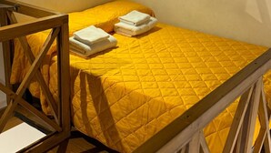 Ein Einzelbett mit gelber Bettdecke, einem Holzkopfteil und einem kleinen Nachttisch.
