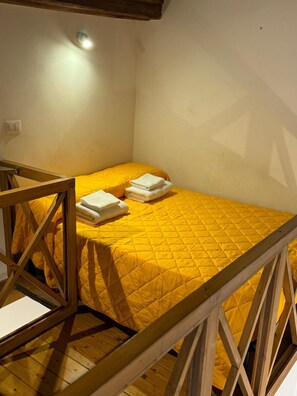 A single bed with a yellow quilt, a wooden headboard, and a small bedside table. - Little House in Trastevere Apartment with Balcony, Wi-Fi and Air Conditioning (Rome)