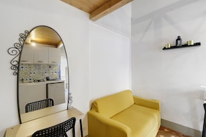 Ein gemütlicher Raum mit Küchenzeile, einem gelben Sofa, einer Holzbalkendecke und einem an der Wand befestigten Regal mit Küchenutensilien.