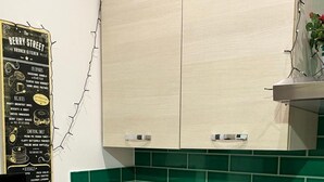 Una cocina con salpicadero de azulejos verdes, un lavamanos de acero inoxidable y una tetera sobre la encimera.