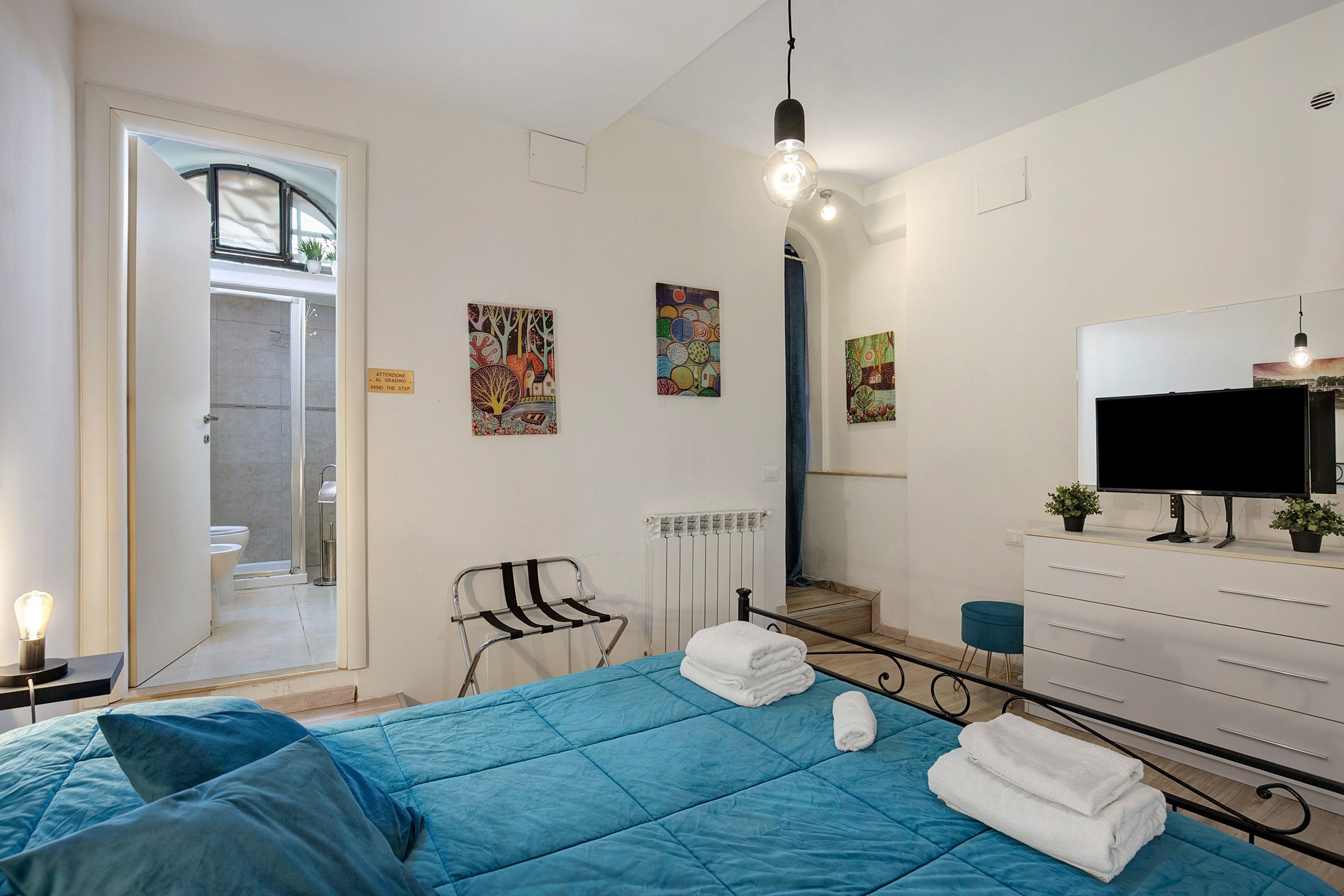 A bedroom with a bed, a TV, a dresser, and artwork on the walls.