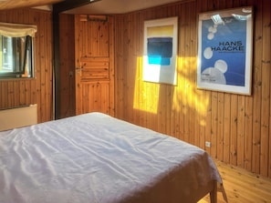 A room with wooden paneling, a bed with a white bedspread, a window with curtains, and a poster on the wall. - Timber house with sauna a few steps from the beach (Rødby)
