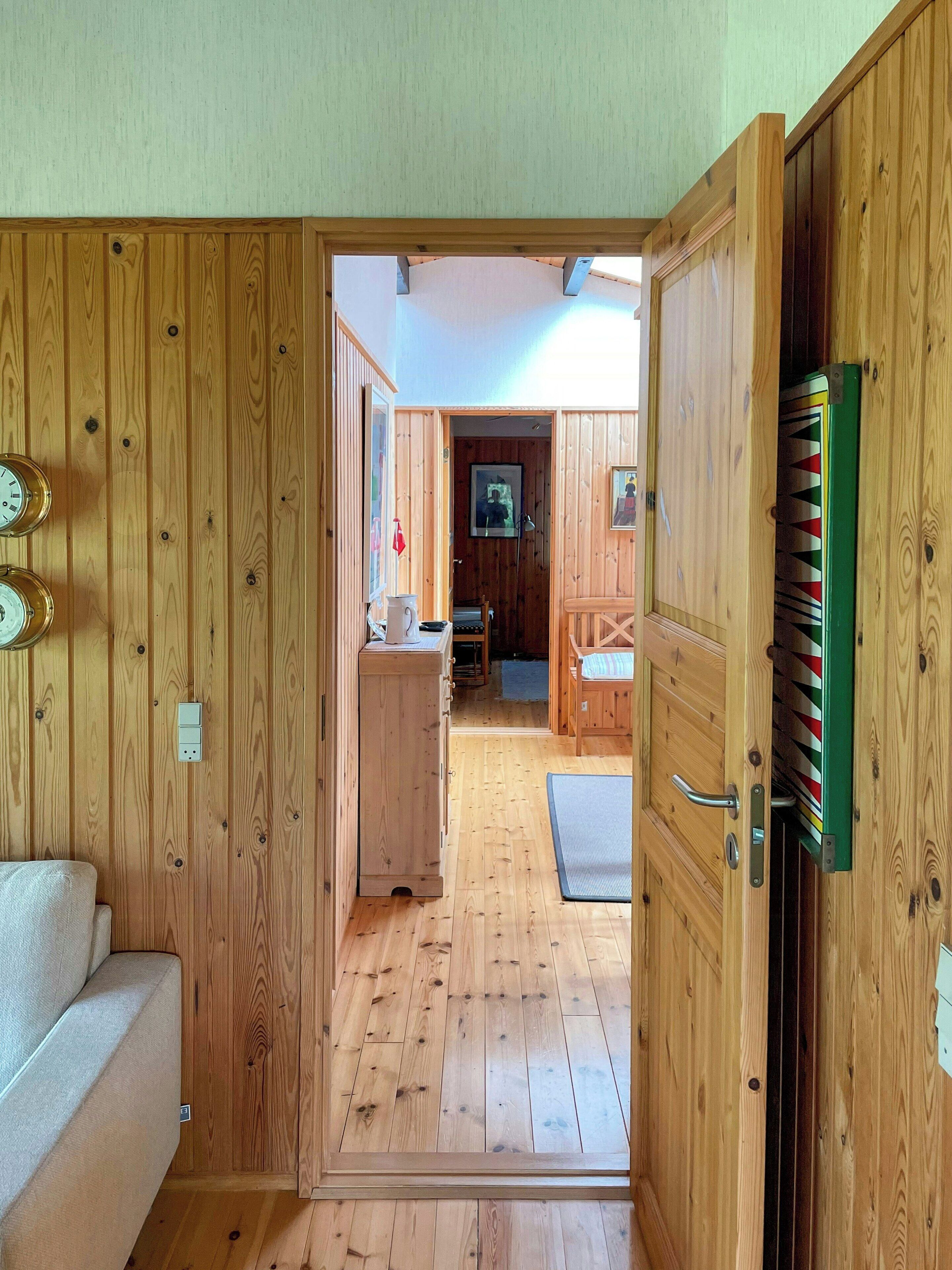 Un interno in legno con un divano, una porta che dà su un'altra stanza e una sveglia appesa al muro.