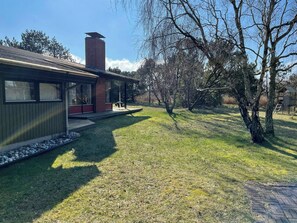 A modern house with a brick chimney, a covered porch, and a well-maintained lawn. - Timber house with sauna a few steps from the beach (Rødby)