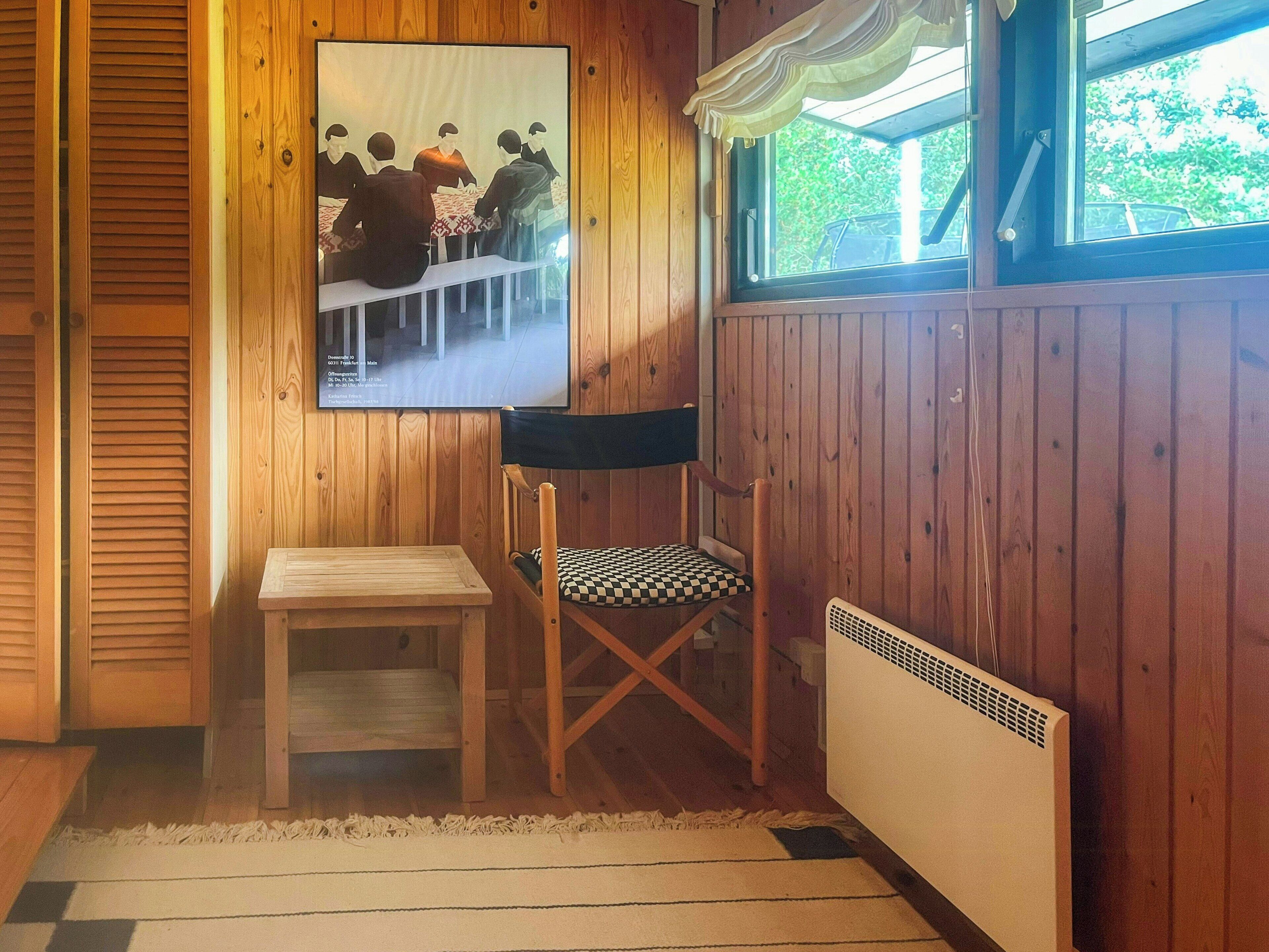 A wooden-paneled room with a table, a chair, a radiator, and a window with a view of greenery.