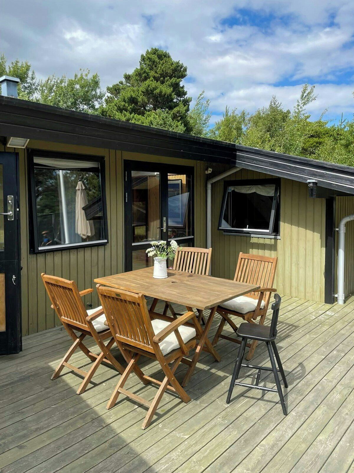 A wooden deck with a table and chairs, a window, and a door.