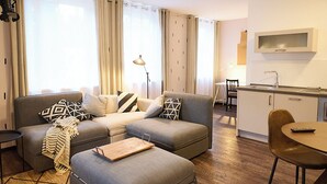Een moderne woonkamer met een zithoek, een pouf en een eethoek met een tafel en stoelen.