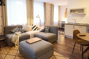 Ein modernes Wohnzimmer mit einer Sofagarnitur, einem Hocker und einem Essbereich mit Tisch und Stühlen.