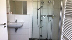 Een badkamer met een douchecabine van glas, een witte wastafel en een spiegel boven de wastafel.