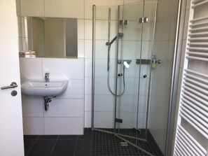 Ein Badezimmer mit einer gläsernen Duschkabine, einem weißen Waschbecken und einem Spiegel darüber.