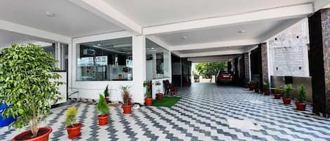 A spacious indoor area with a checkered floor, potted plants, and a red car parked outside.