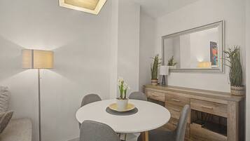 Un moderno comedor con una mesa redonda, sillas grises, una lámpara de pie, un espejo y un aparador con objetos decorativos.