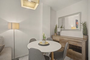 A modern dining area with a round table, grey chairs, a floor lamp, a mirror, and a cabinet with decorative items.