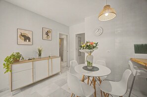 A modern kitchen with white cabinetry, a dining table with chairs, a hanging light fixture, and a clock on the wall.
