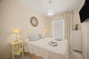A hotel room with a bed, two bedside lamps, a TV, a mirror, and a window with curtains.
