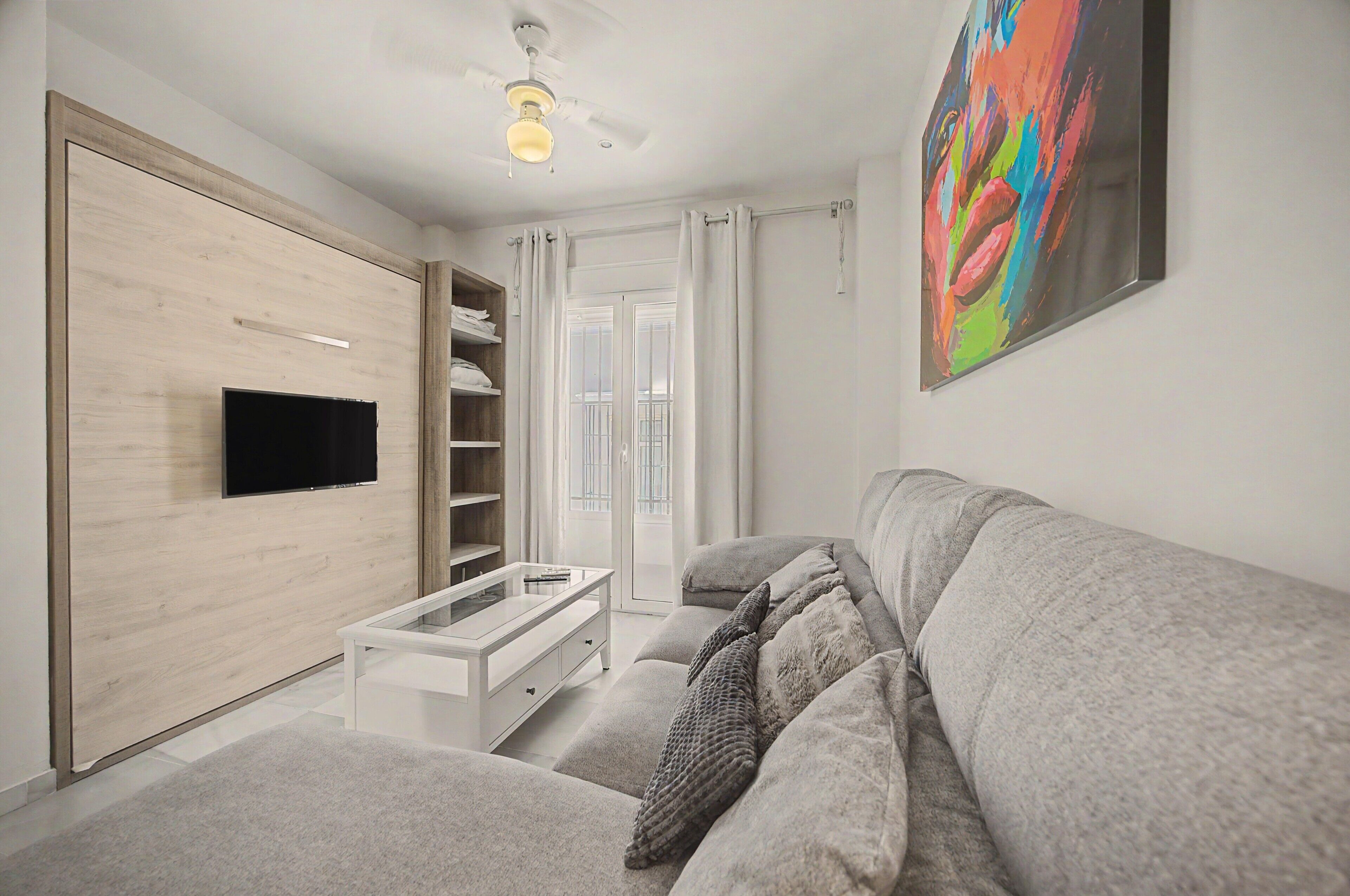 Een moderne woonkamer met een flatscreen televisie, een witte bank, een glazen salontafel en een plafondventilator.
