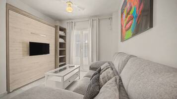 Een moderne woonkamer met een flatscreen televisie, een witte bank, een glazen salontafel en een plafondventilator.