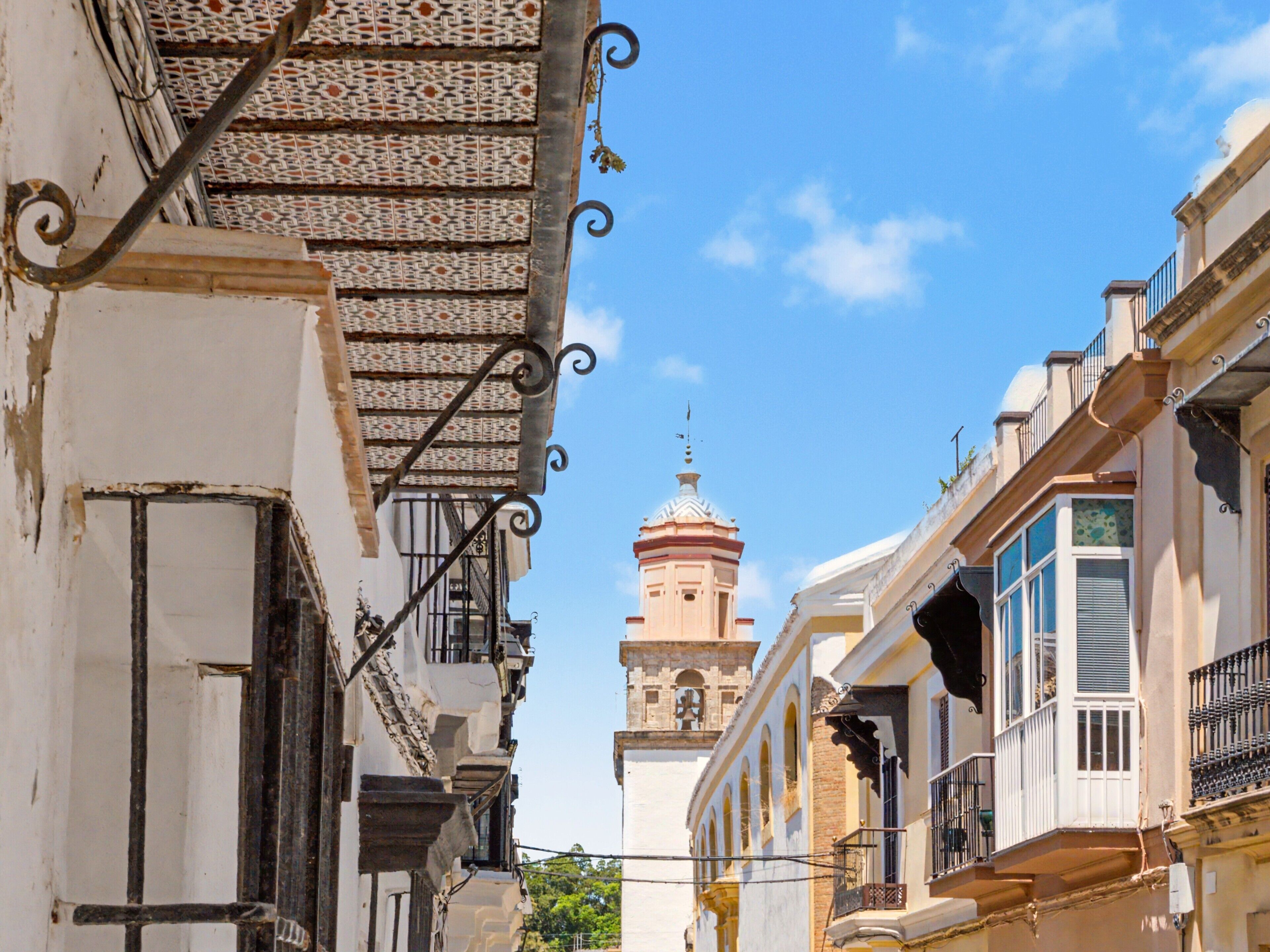 A narrow street with buildings on either side, a tower in the distance, and a clear blue sky.