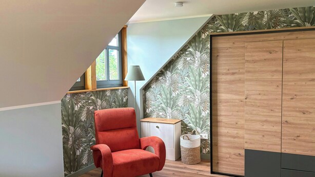 A room with a sloped ceiling, a red chair, a small white cabinet, a woven basket, and a wooden wardrobe. - Holiday home on Lake Ternscher with private jetty (Selm)