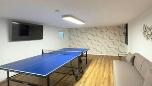 A ping pong table in a room with a wooden floor, a sofa, and a wall with a circular pattern. - Holiday home on Lake Ternscher with private jetty (Selm)
