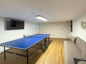 A ping pong table in a room with a wooden floor, a sofa, and a wall with a circular pattern. - Holiday home on Lake Ternscher with private jetty (Selm)
