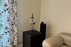 A room with a black square table, a glass-top table lamp, a beige sofa, and a floral-patterned curtain. - [Casa Mafalda] Design Home/Portovenere-5Terre+A/C (Portovenere)
